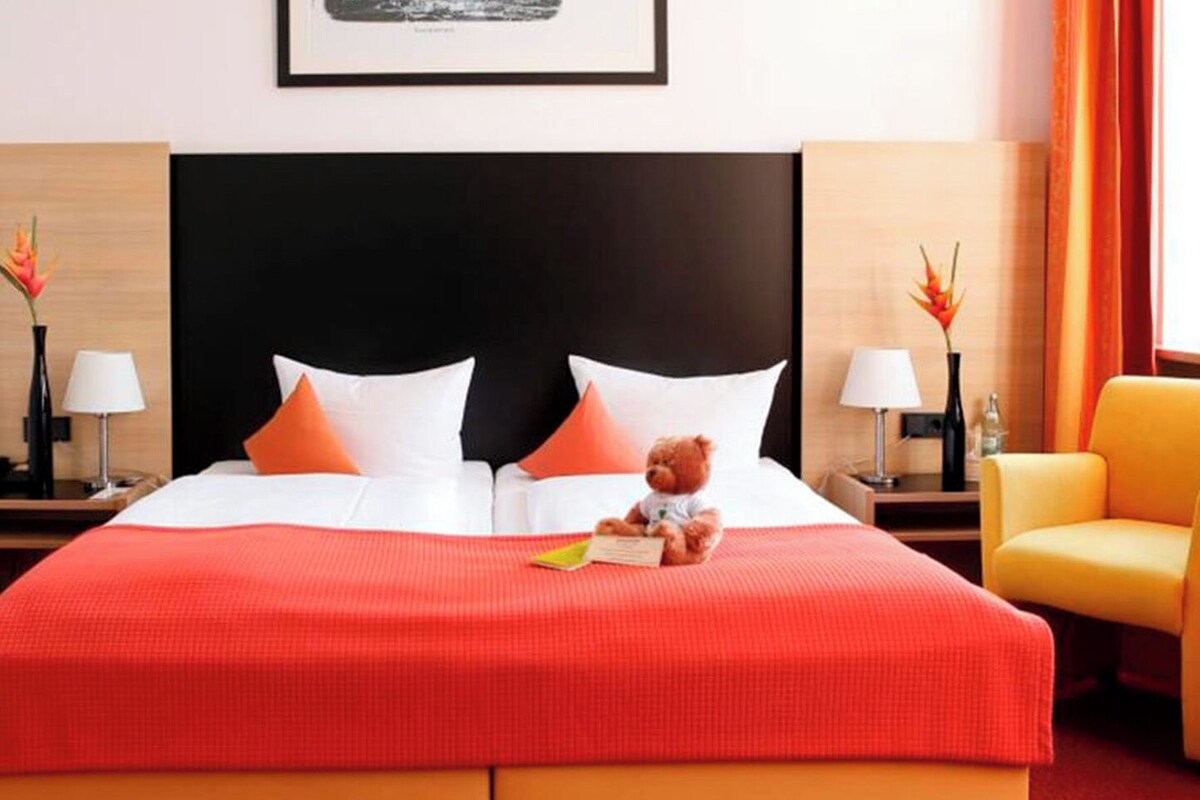 A hotel room with a large bed, two nightstands, a chair, and a window with curtains.
