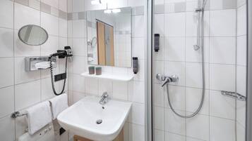 Un baño moderno con lavamanos, espejo, toallero y cabina de ducha con mampara de vidrio.