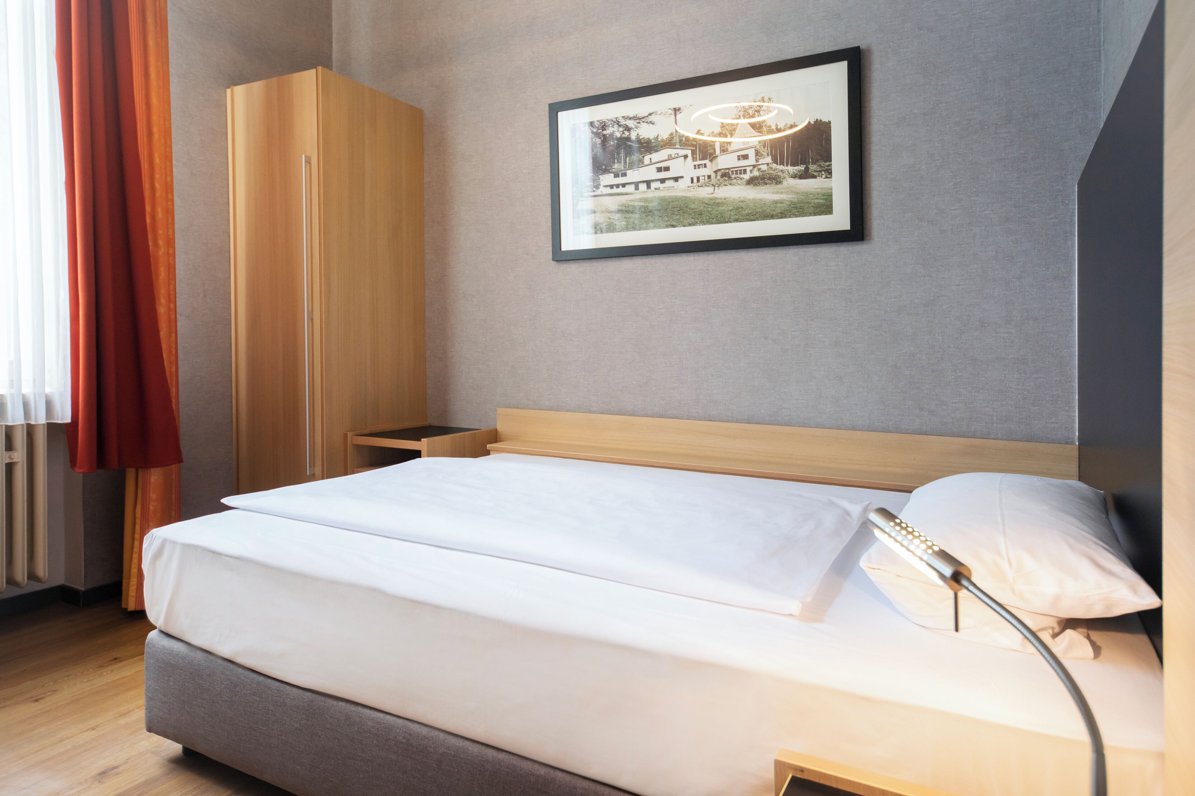 A neatly made bed with a headboard, a bedside table, a wardrobe, and a framed picture on the wall.