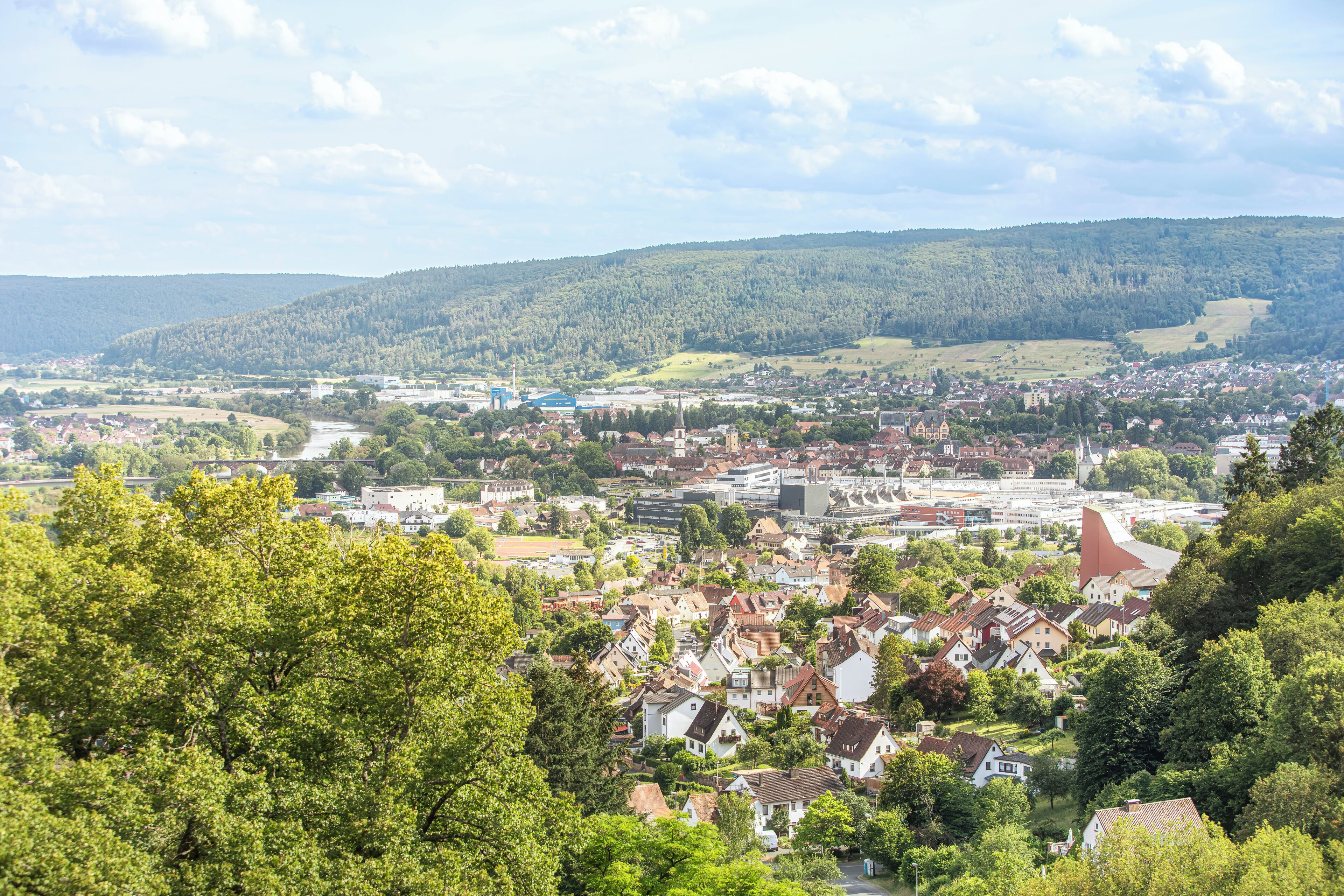 A town with a mix of residential and commercial buildings, surrounded by green hills.