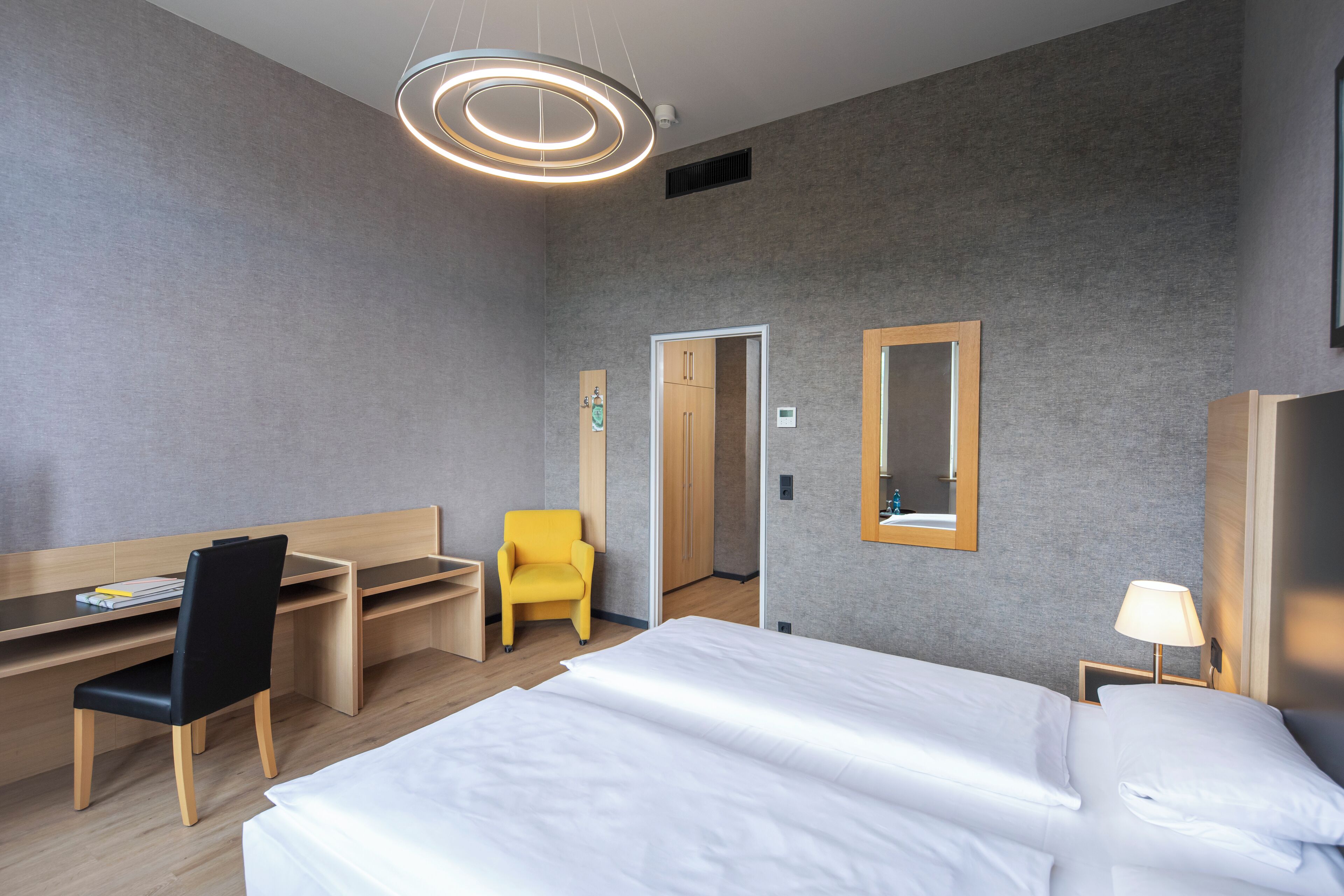 Ein modernes Hotelzimmer mit einem großen Bett, einem Schreibtisch mit Stuhl, einem kleinen Tisch und einem Spiegel.
