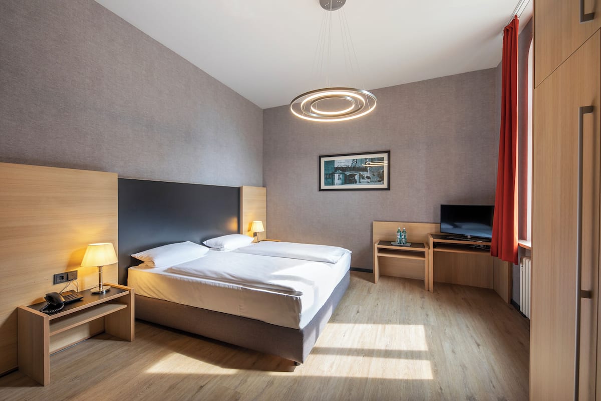 Una habitación de hotel moderna con cama, mesitas de noche, un escritorio, televisor y una cortina roja.