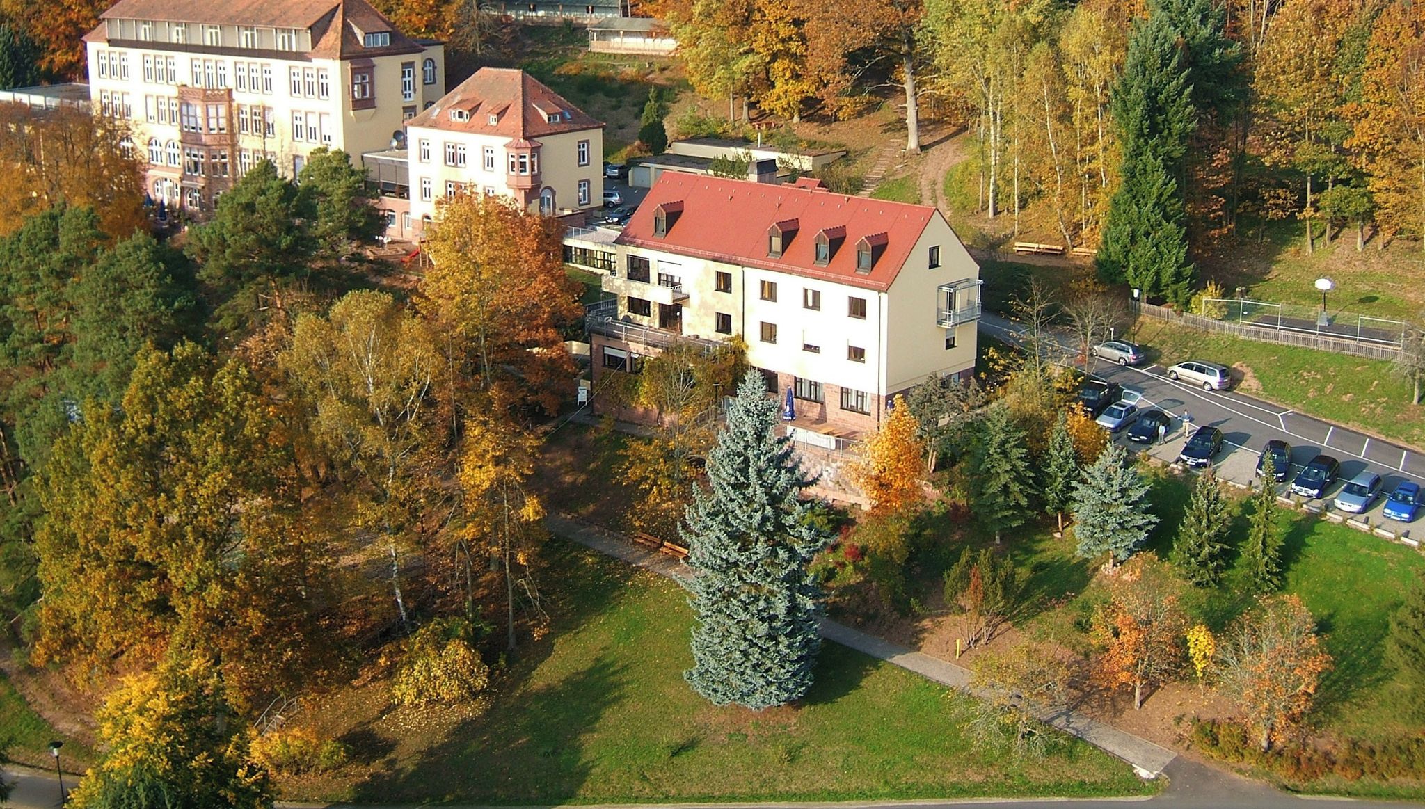 Ein mehrstöckiges Gebäude mit rotem Dach, umgeben von Bäumen in Herbstfarben.