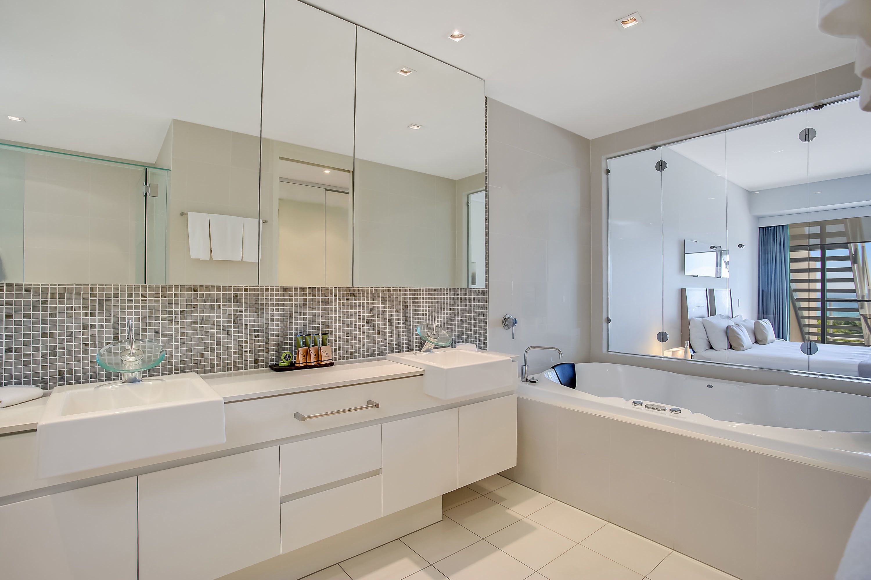 Een moderne badkamer met een grote spiegel, twee wasbakken, een badkuip en een betegelde achterwand.