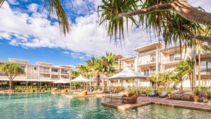 A hotel with a swimming pool, lounge chairs, and palm trees. - Peppers Salt Resort & Spa (Kingscliff)