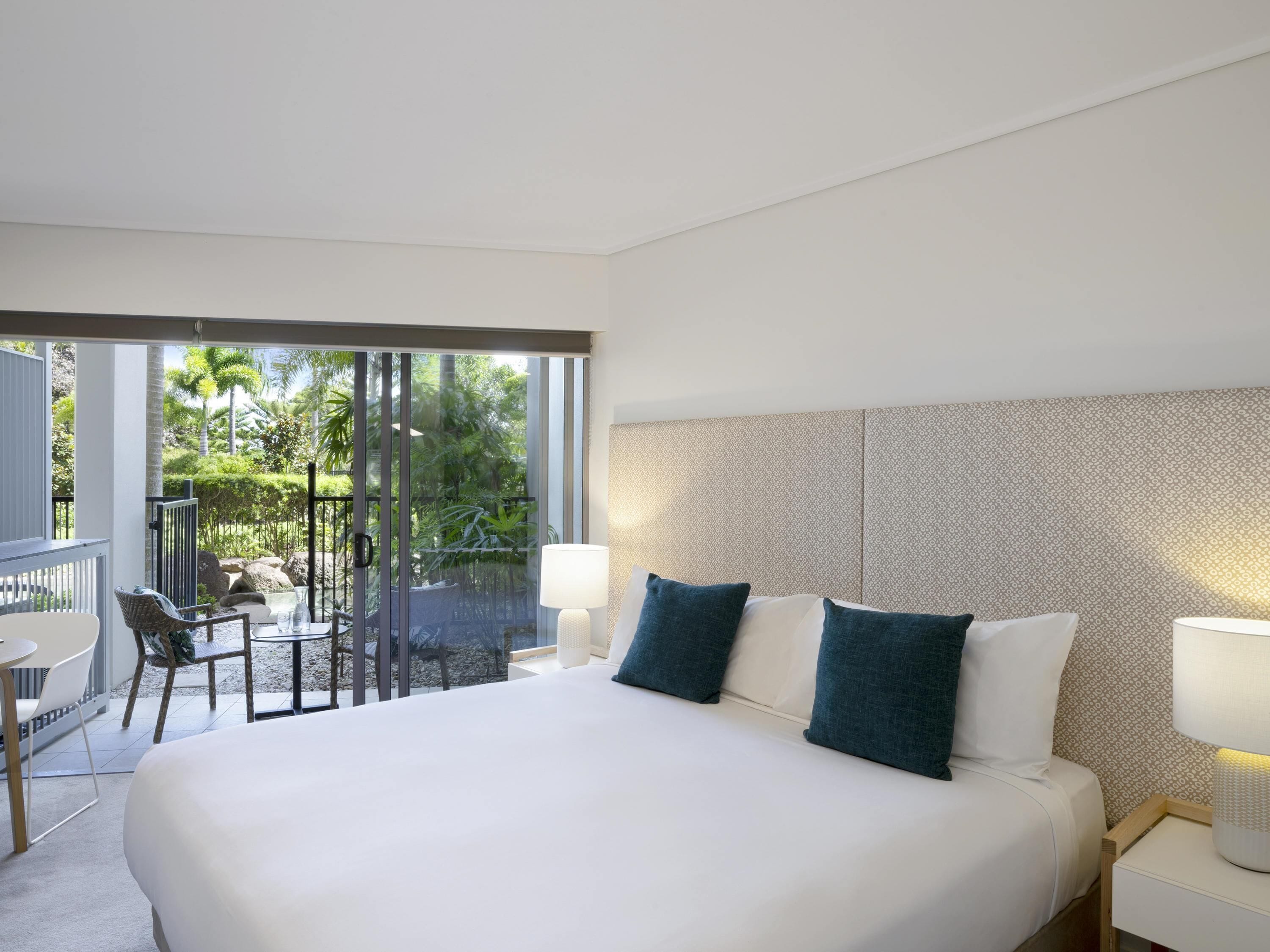 Een hotelkamer met een groot bed, twee bedlampen, een gestreept hoofdeinde en een balkon met tuinmeubels.