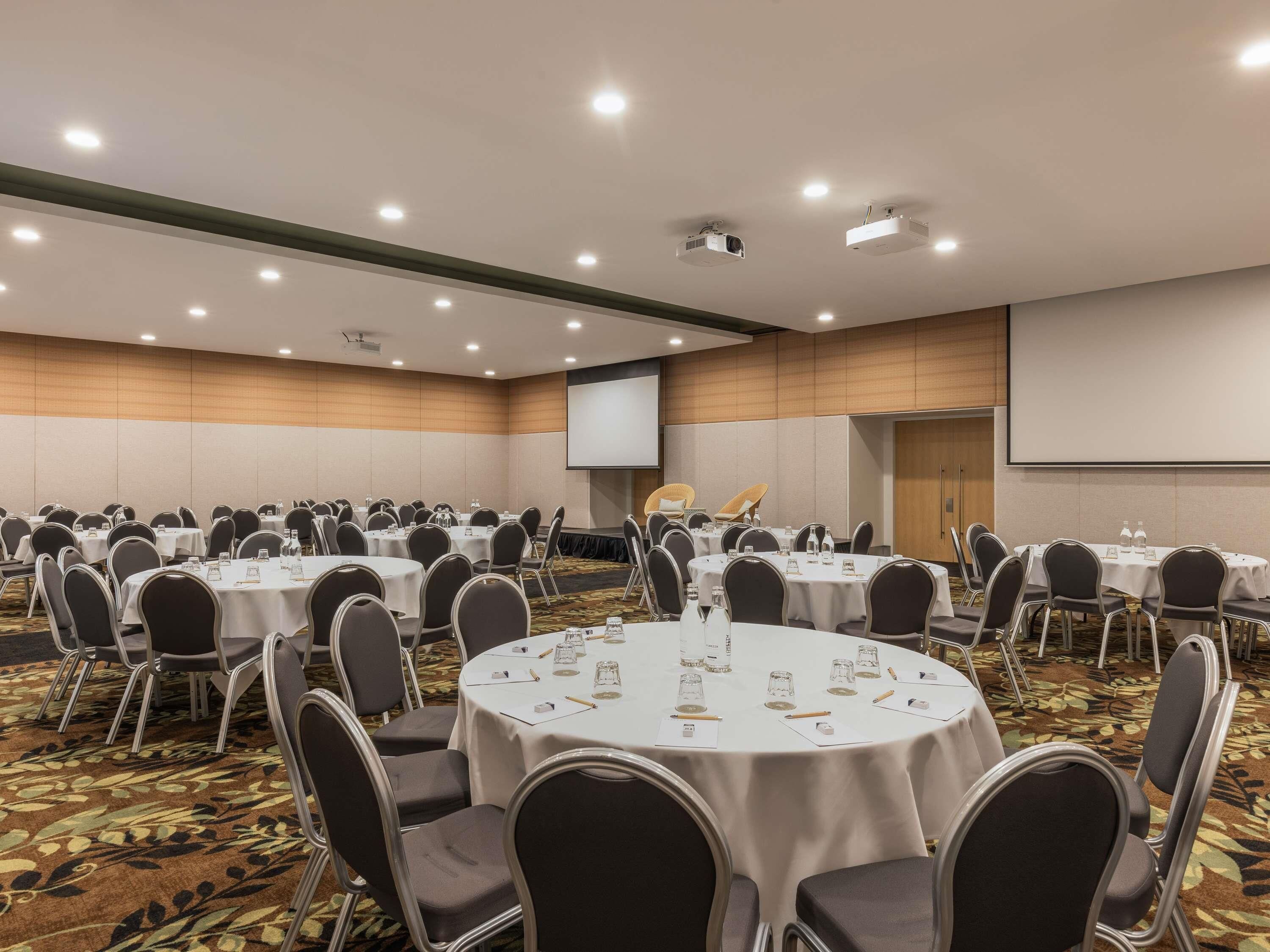 A conference room with round tables, chairs, and a projector screen.