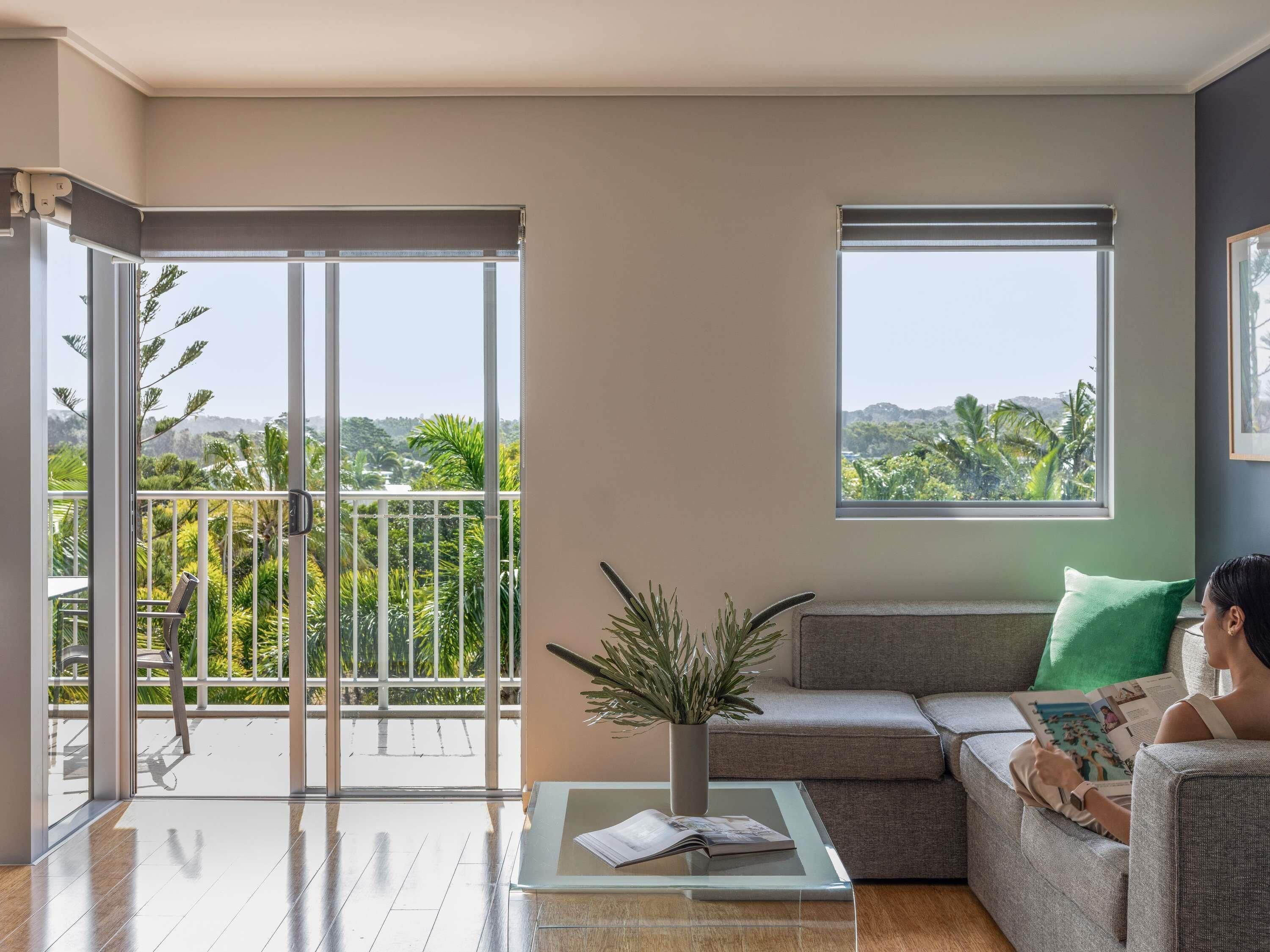 A modern living room with a balcony, a sofa, a coffee table, and a view of greenery.