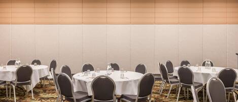 A conference room with round tables, chairs, and a carpeted floor.