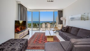 A modern living room with a large TV, a sofa, a coffee table, and a view of the ocean. - Peppers Salt Resort & Spa (Kingscliff)