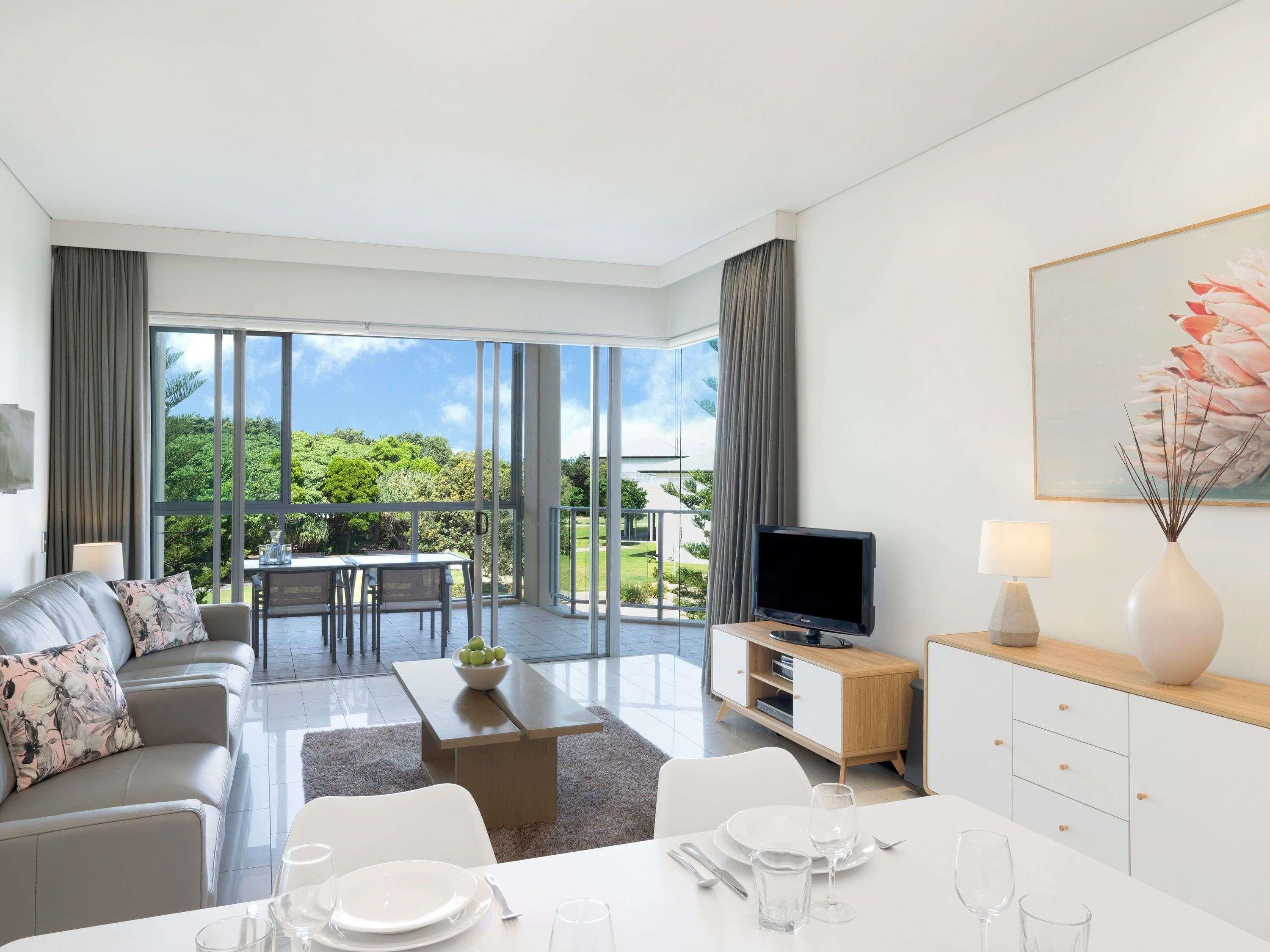 Un salon moderne comprenant un canapé, une table à manger, un téléviseur et un balcon offrant une vue sur la verdure.