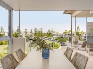 Een balkon met rieten stoelen, een tafel en een blauwe vaas met planten.