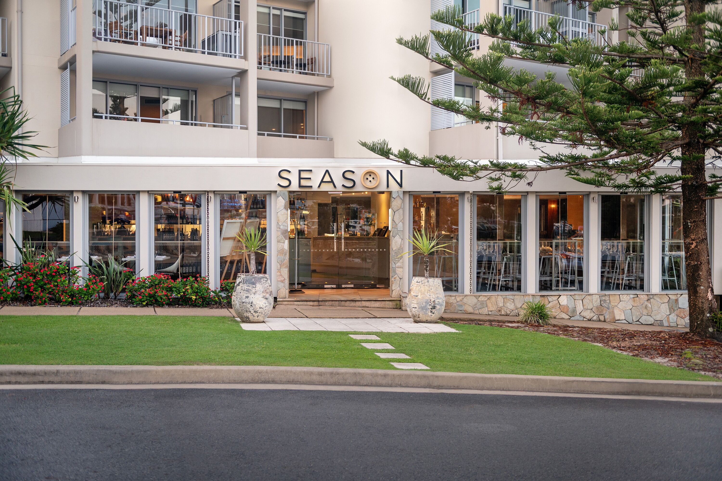 Un bâtiment sur lequel on peut lire l’inscription « SEASON », et un restaurant dont on aperçoit les tables en terrasse à travers les fenêtres.
