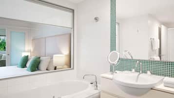 A modern bathroom with a large bathtub, a sink with a mirror, and a window overlooking a bedroom.