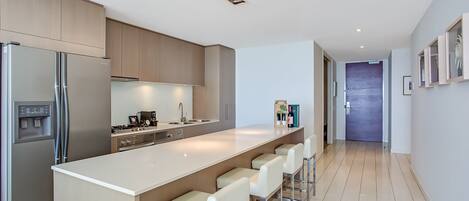 A modern kitchen with a central island, stainless steel appliances, and a long countertop.