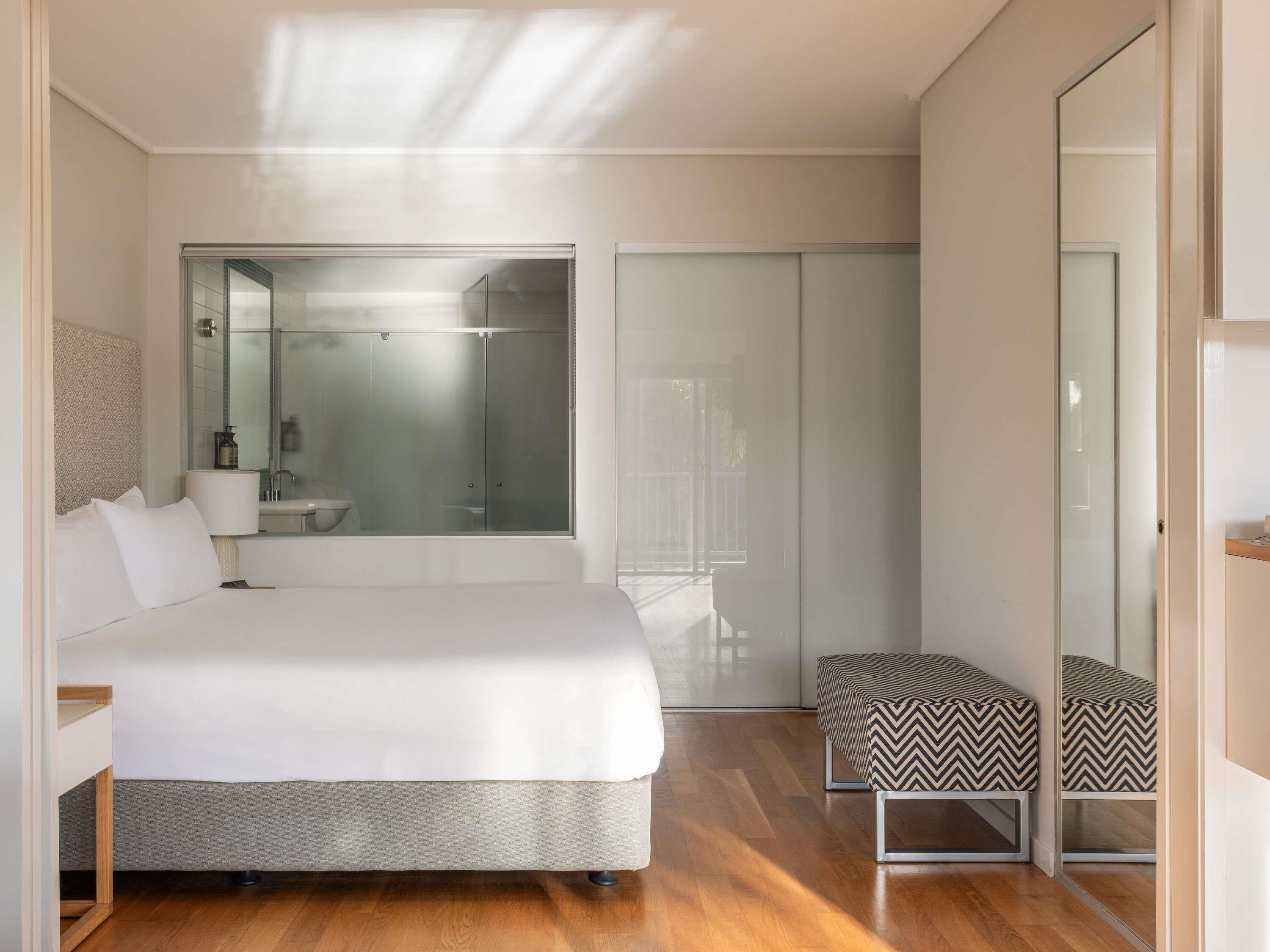 Een moderne slaapkamer met een groot bed, een bankje, een douchecabine van glas en uitzicht op het omliggende landschap.
