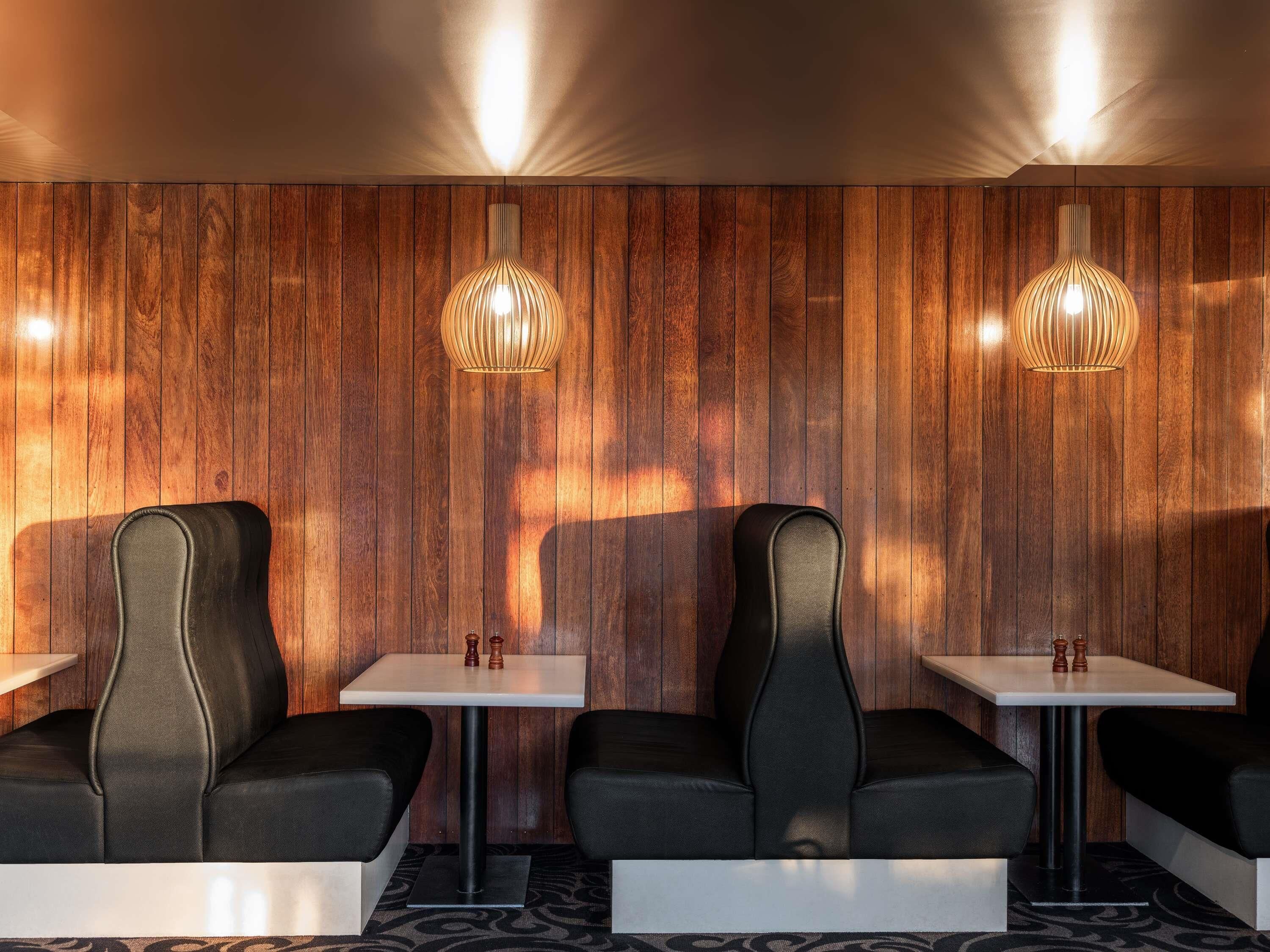 Un intérieur moderne avec des murs lambrés en bois, des fauteuils en cuir noir et des tables blanches.