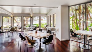 A spacious dining area with multiple tables and chairs, large windows offering views of greenery and a street. - Peppers Salt Resort & Spa (Kingscliff)