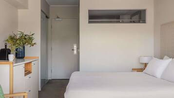 Een hotelkamer met een bed, een bureau met een plant, een lamp en uitzicht op de gang.