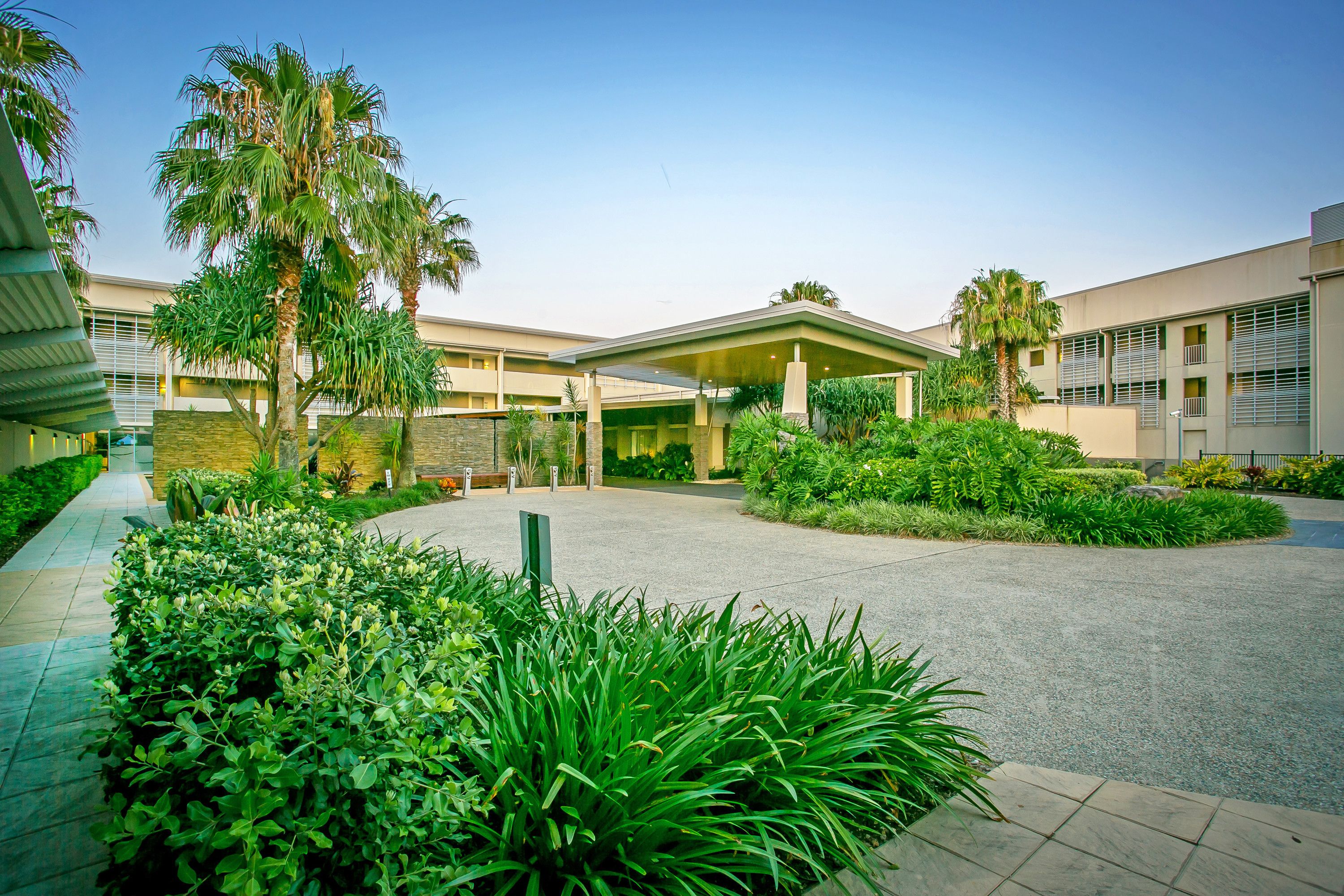 A modern building with a covered entrance, surrounded by lush greenery and palm trees.
