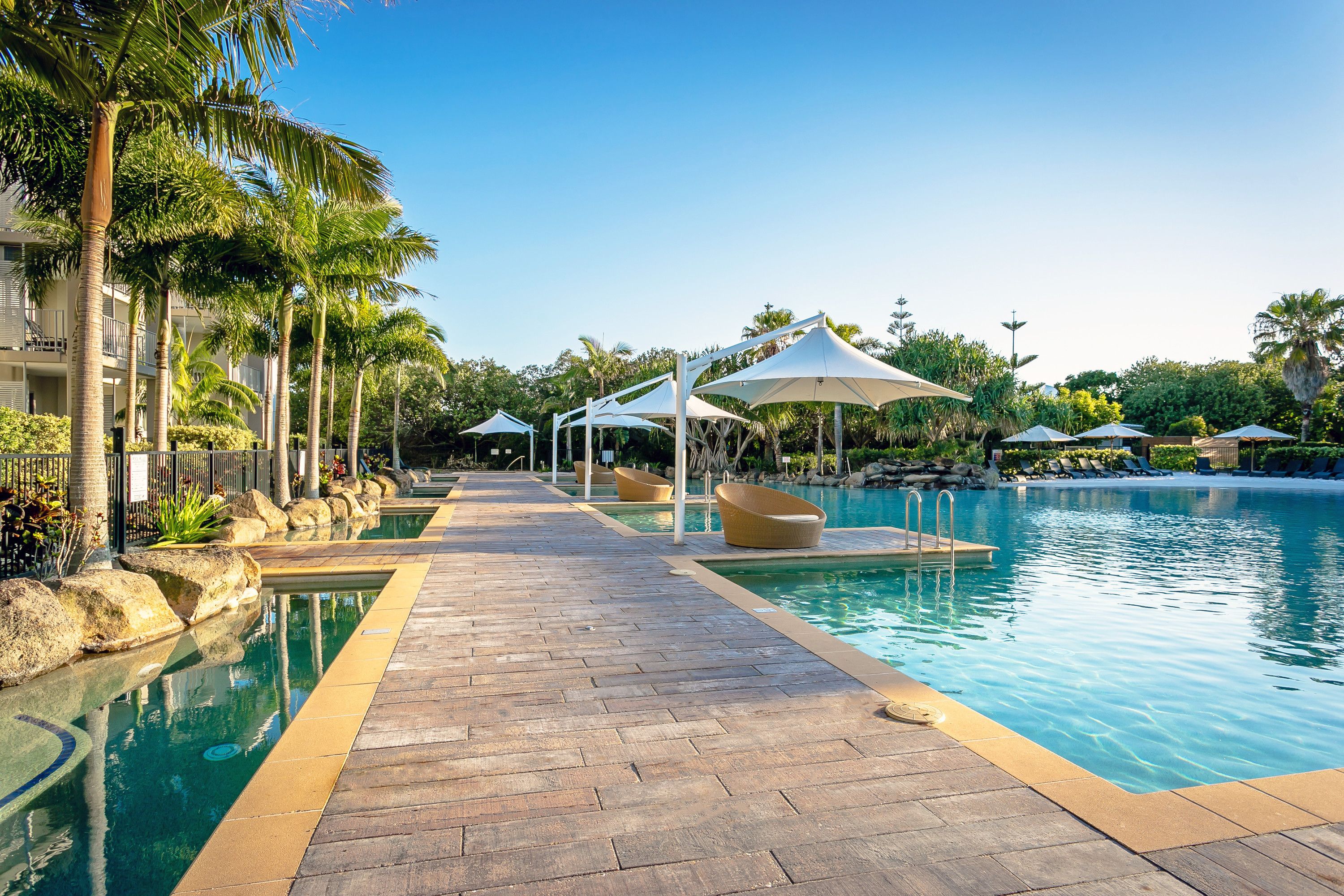 A pool area with a wooden deck, lounge chairs, and umbrellas.