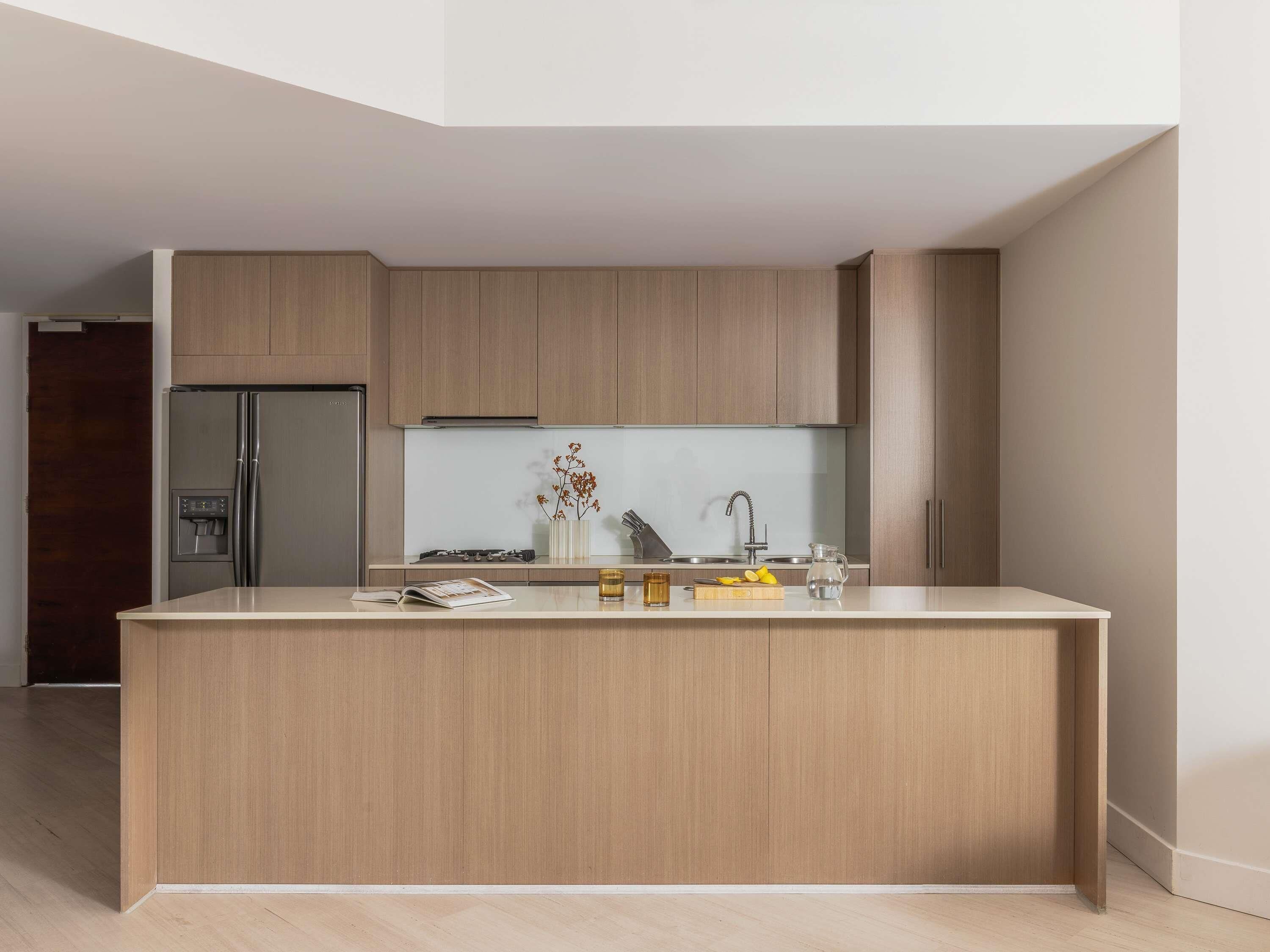 A modern kitchen with wooden cabinetry, a built-in refrigerator, a central island, and a backsplash.