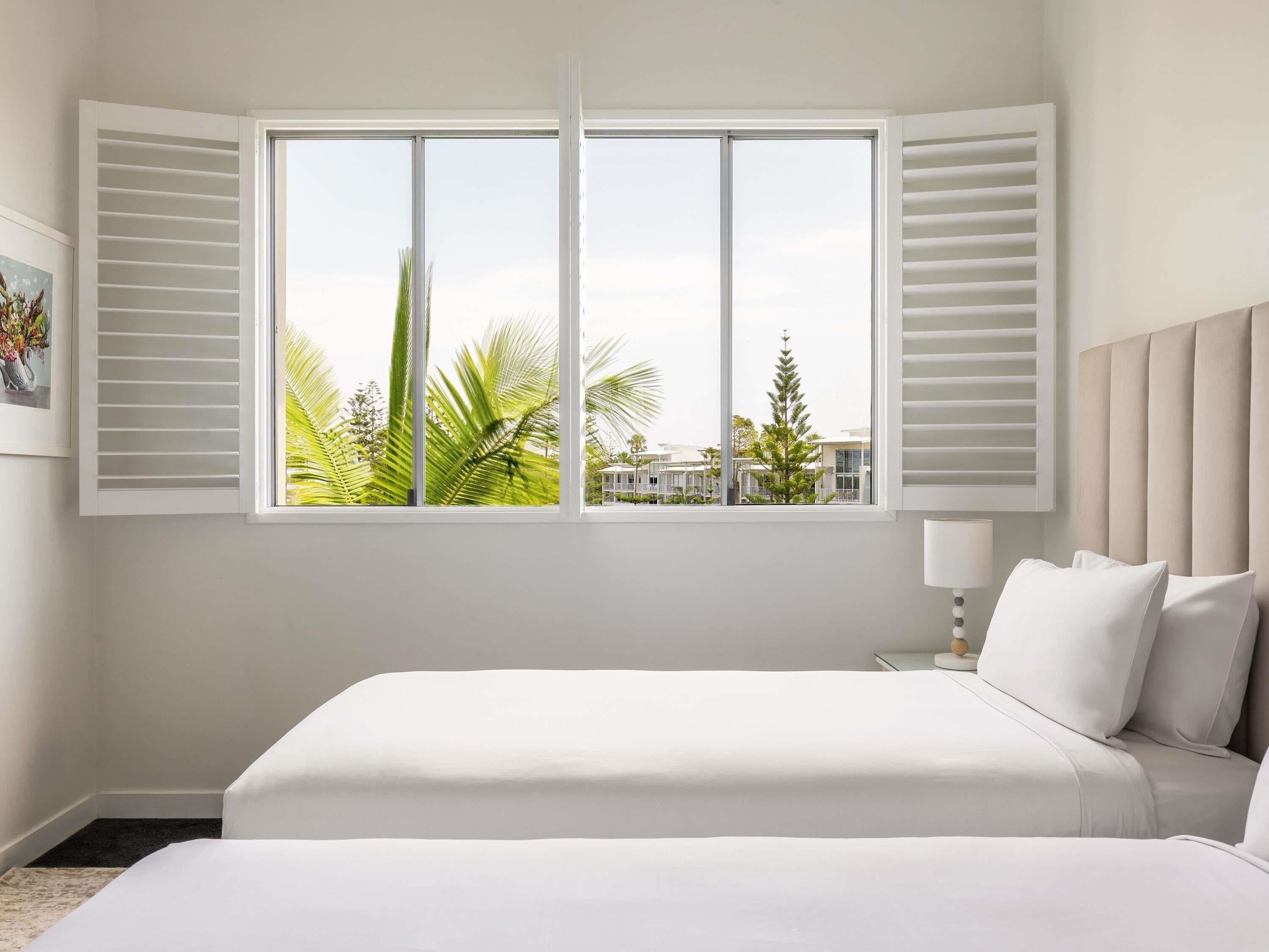 A hotel room with a large window, a bed, a nightstand, and a lamp.