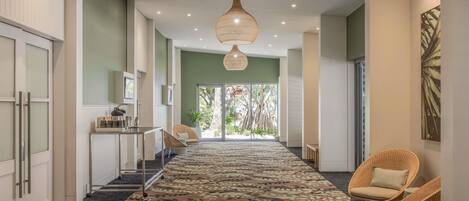 A hallway with a patterned carpet, wicker chairs, a hanging light fixture, and a view through glass doors.