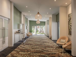 A hallway with a patterned carpet, wicker chairs, a hanging light fixture, and a view through glass doors.