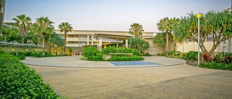 A spacious courtyard with a central circular area, surrounded by palm trees and well-maintained greenery.