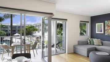 A modern living room with a balcony, a grey sofa, and a dining area with a table set for four.