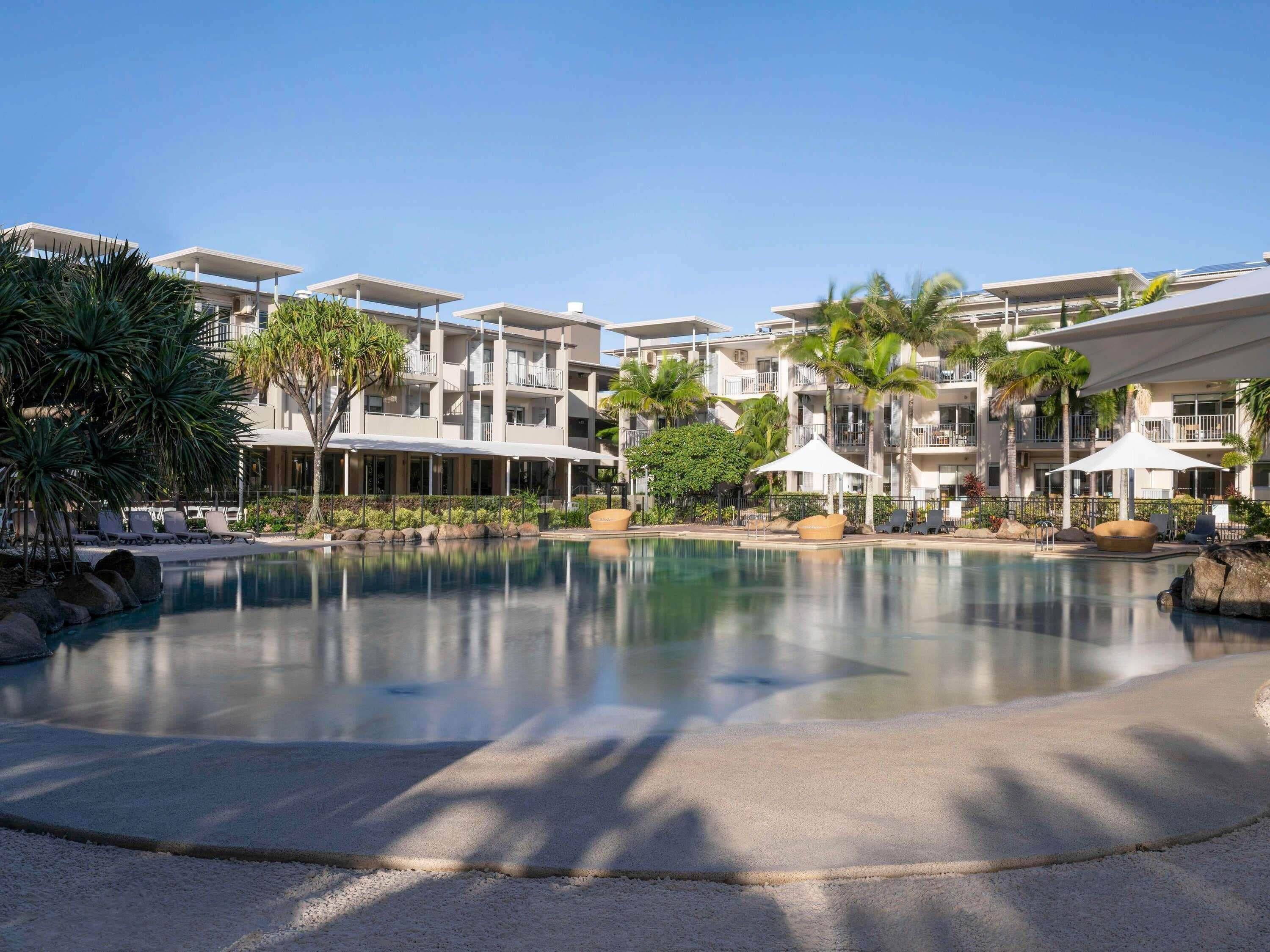 A resort with a swimming pool, palm trees, and multi-story buildings.