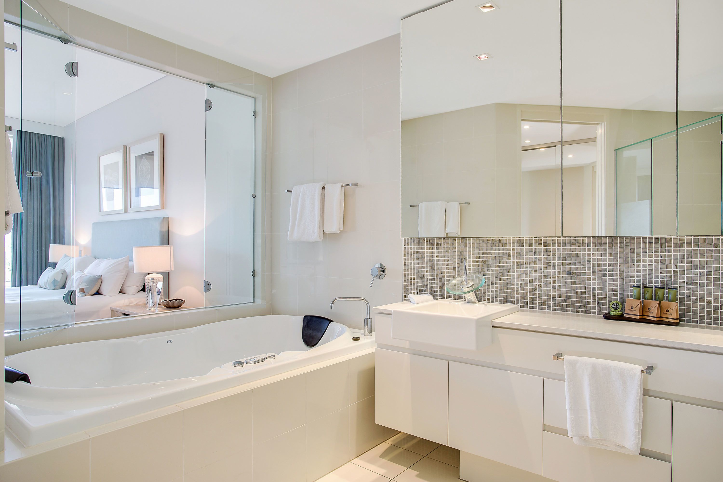 A modern bathroom with a large bathtub, a vanity with a mirror, and a tiled backsplash.