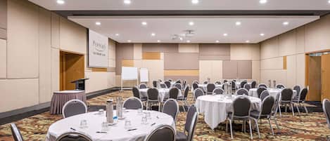 A conference room with multiple round tables, chairs, a podium, and a presentation screen.