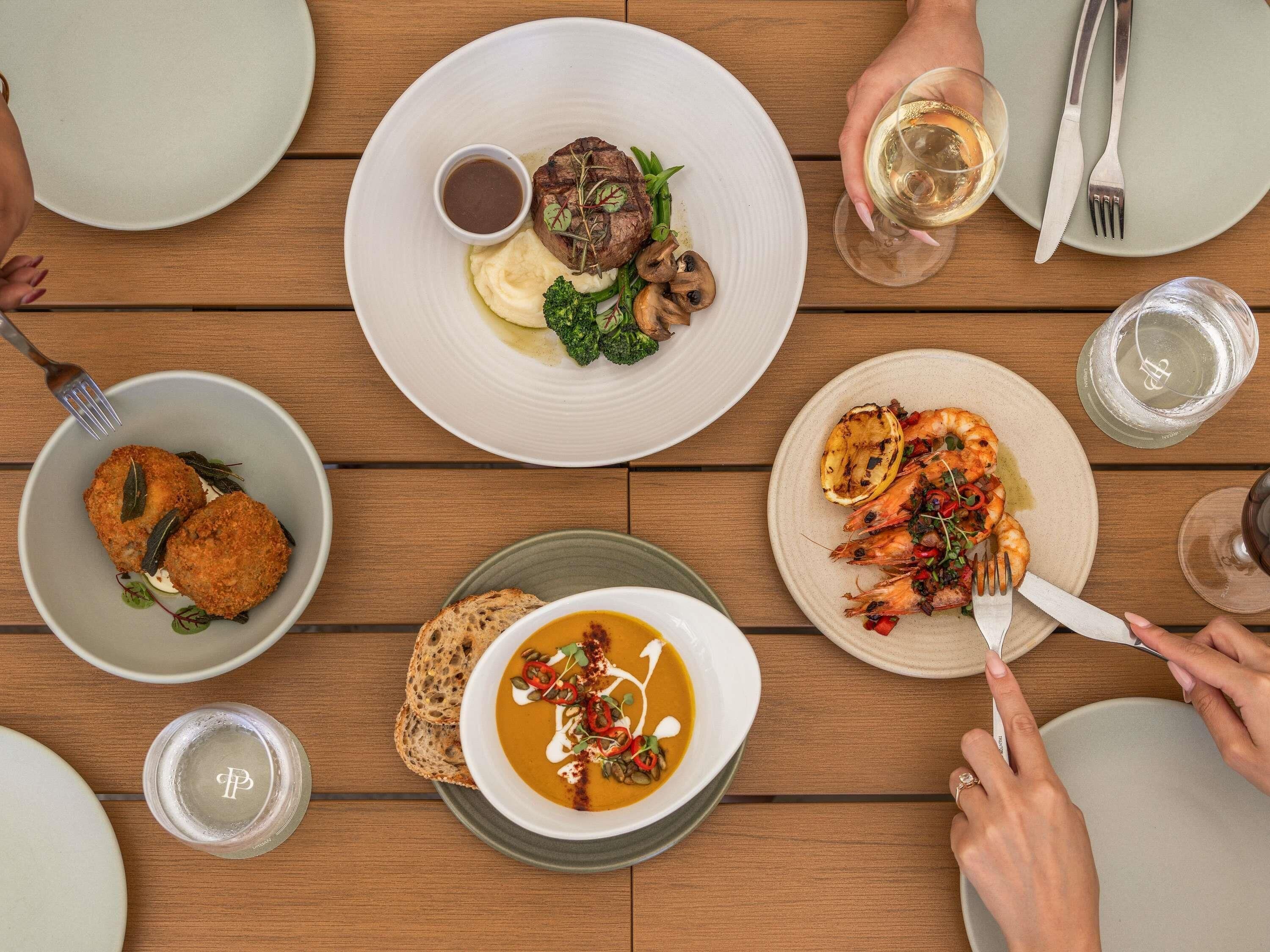 Una mesa de comedor con platos de comida, cubiertos y vasos.