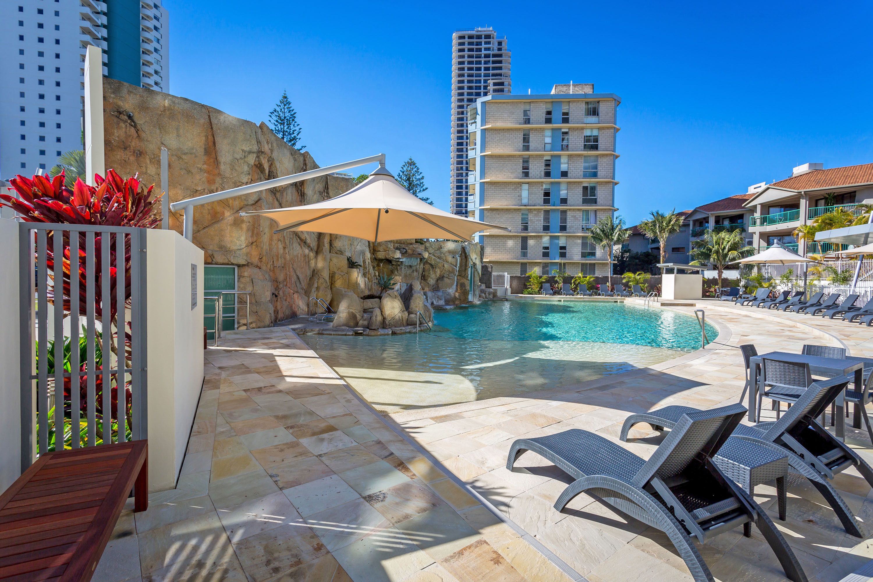 A pool area with lounge chairs, a rock formation, and a tall building in the background.