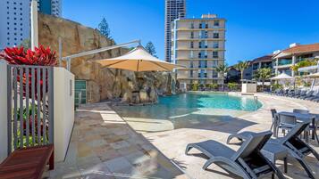 A pool area with lounge chairs, a rock formation, and a tall building in the background.
