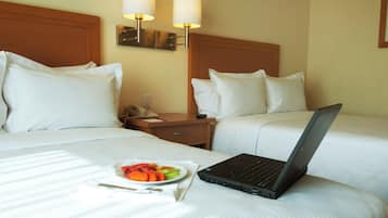 A hotel room with two beds, a laptop on one bed, and a plate of fruit on the bed.