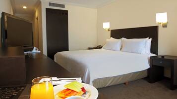 Habitación de hotel con cama, mesita de noche y escritorio con una computadora portátil y un plato de desayuno.