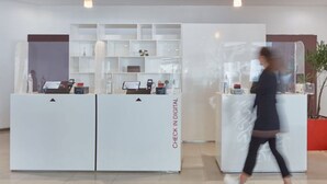 Ein Empfangsbereich mit zwei Check-in-Schaltern, einem digitalen Anzeigetafel und einer Zimmerpflanze.