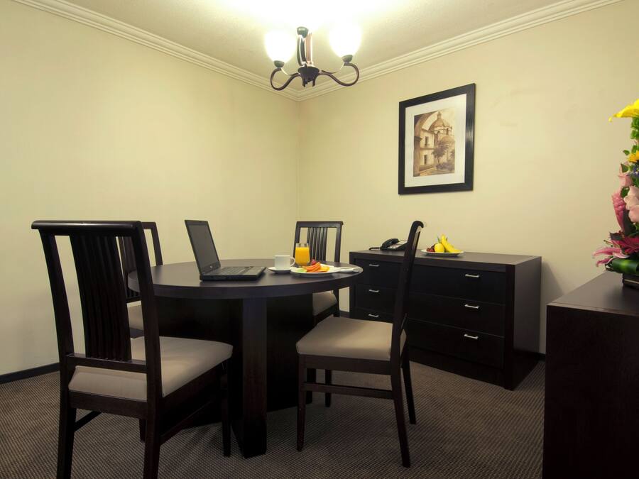 A small, private dining area with a round table, two chairs, a laptop, a phone, and a vase of flowers.