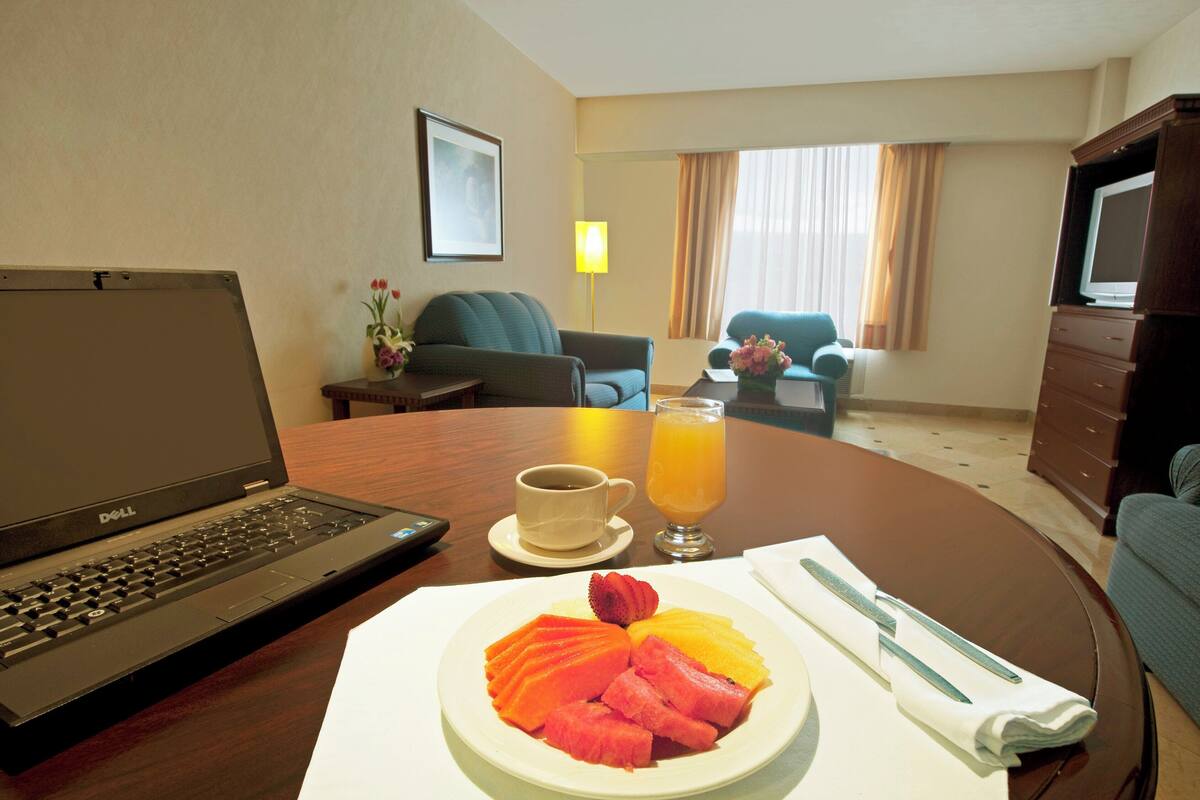 A hotel room with a laptop, breakfast plate, coffee, and juice on the table.