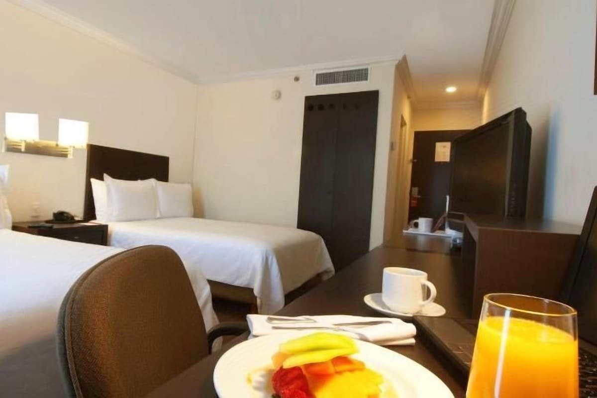 A hotel room with two beds, a dining table with breakfast, and a TV.