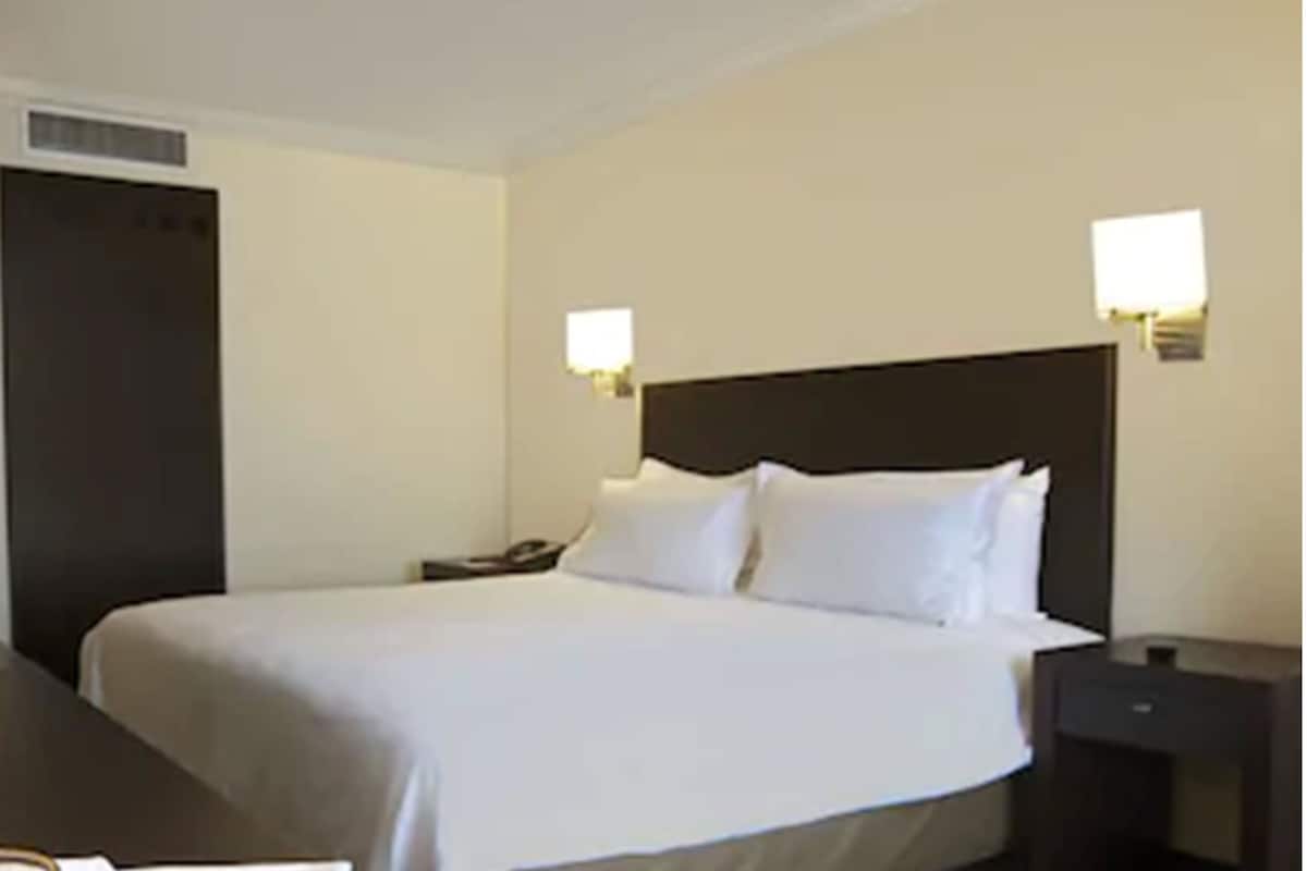 Una habitación de hotel con una cama grande, dos mesitas de noche y dos lámparas de pared.