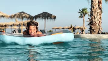 Una persona galleggia in piscina con vista sulle palme e sugli ombrelloni sullo sfondo.
