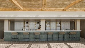 A bar area with a concrete countertop, four bar stools, and shelves stocked with bottles. - Mitsis Norida (Kos)