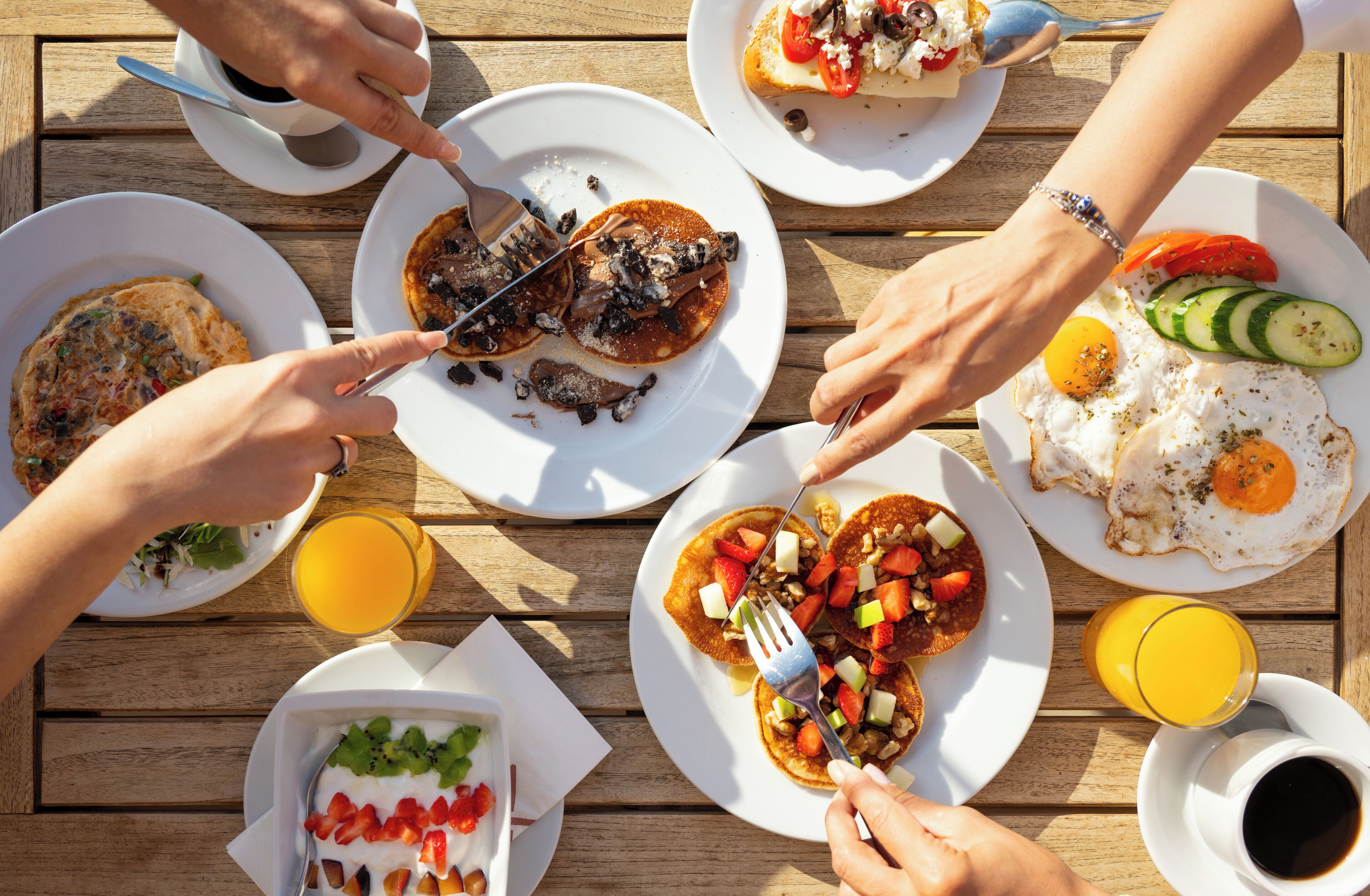 Uma mesa de madeira com diversos pratos de café da manhã, incluindo panquecas, ovos e frutas.