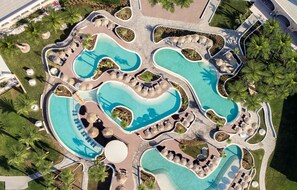 An aerial view of a resort with multiple interconnected swimming pools, lounge areas, and palm trees. - Mitsis Norida (Kos)