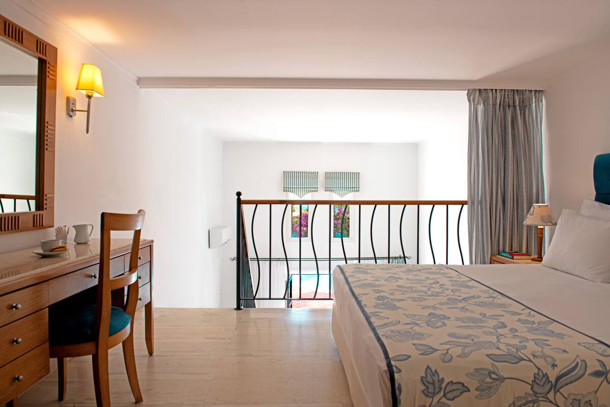 Ein Hotelzimmer mit Bett, Schreibtisch mit Stuhl, einer Lampe und Blick ins Freie.