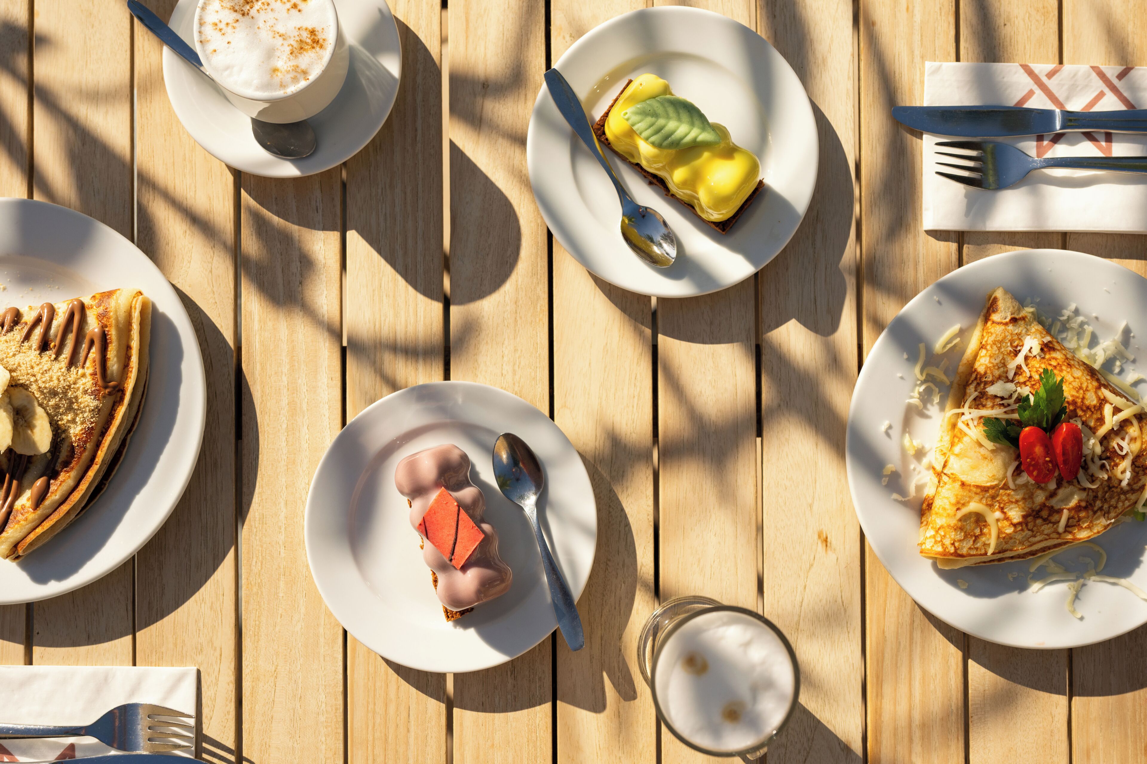 A wooden table with plates of food, utensils, and a glass of milk.